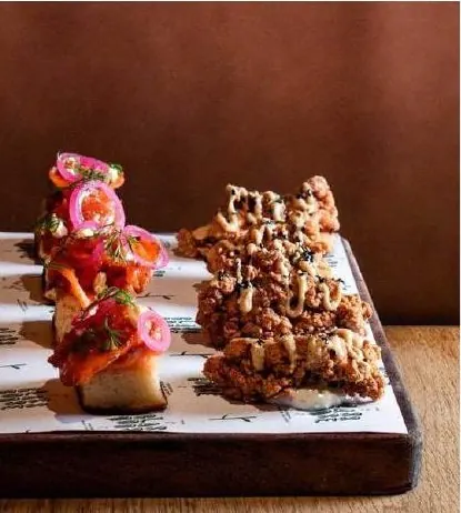 Canapés on a wooden board: crostini with pickled onion and fried chicken pieces.